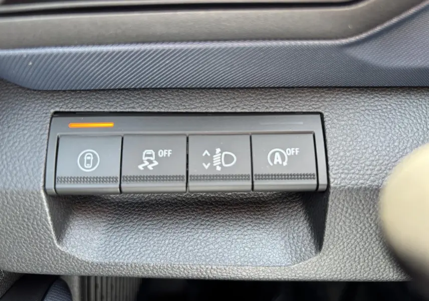 Gros plan sur les boutons de commande noirs du tableau de bord du Dacia Duster 2025, finition Journey, avec témoin orange allumé.