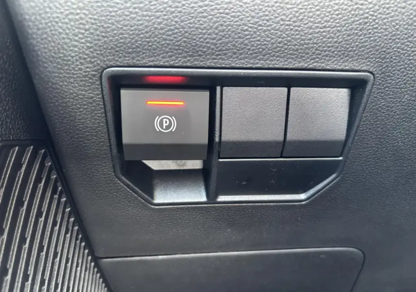 Gros plan sur le bouton de frein de stationnement électrique avec témoin rouge dans l'habitacle du Dacia Duster 2025.