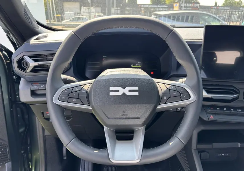 Volant noir du Dacia Duster 2025 vu de face, avec commandes intégrées et tableau de bord digital en arrière-plan.
