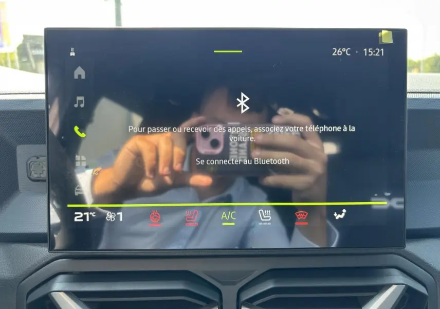 Écran tactile central du tableau de bord du Dacia Duster III vert cèdre, affichant la connexion Bluetooth et commandes climatisation.