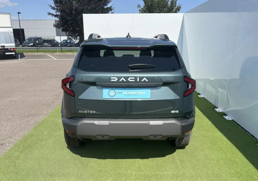 Vue arrière du Dacia Duster III vert cèdre métallisé avec logo DACIA blanc et feux arrière en forme de flèche.