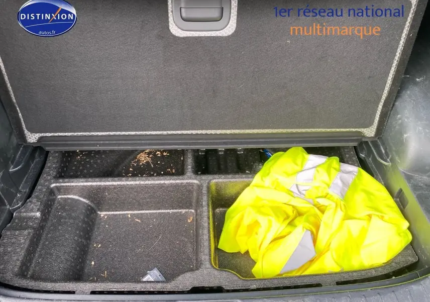 Compartiment de rangement ouvert dans le coffre d'un KIA SPORTAGE noir, avec un gilet jaune visible à droite.