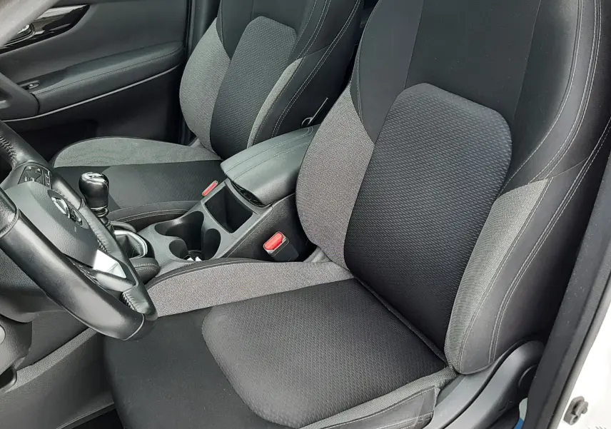 Intérieur du Nissan Qashqai blanc 2020, vue rapprochée sur les sièges avant en tissu noir et gris avec console centrale.