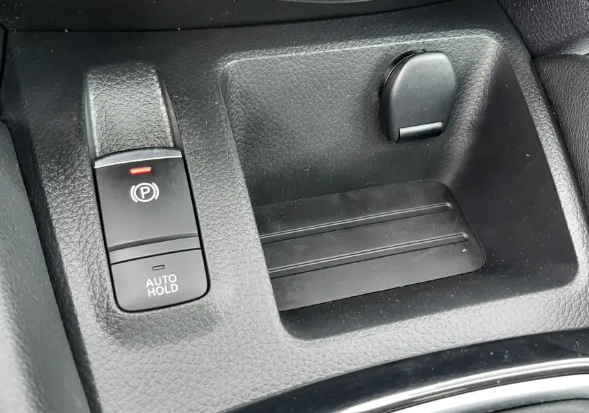 Gros plan sur la console centrale noire du Nissan Qashqai 1.5 DCI 115CH N-Connecta avec frein à main électronique et rangement.
