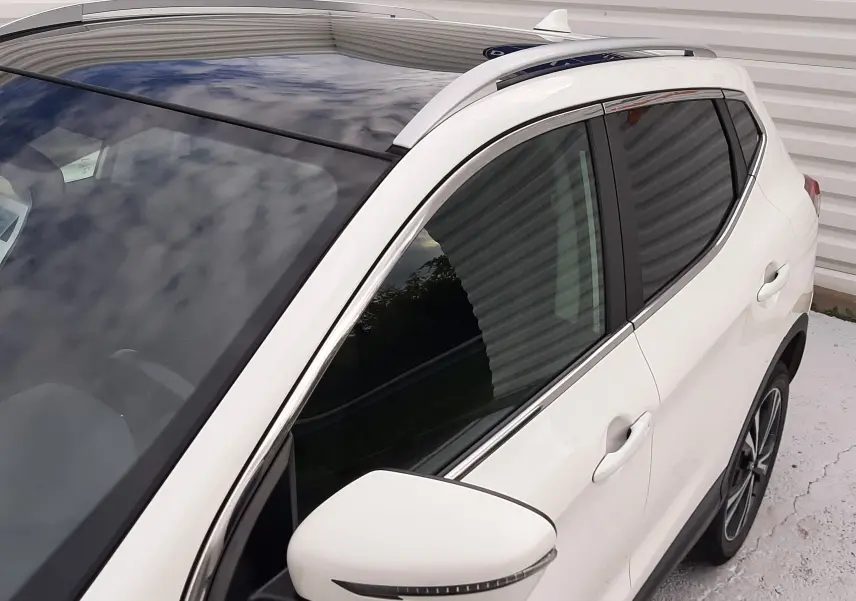 Vue 3/4 avant droit du Nissan Qashqai blanc 2020 avec toit panoramique et rétroviseur latéral intégré.