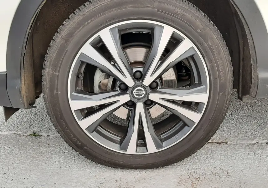 Gros plan sur la roue avant droite d'un Nissan Qashqai blanc, jante alliage bicolore au design moderne.