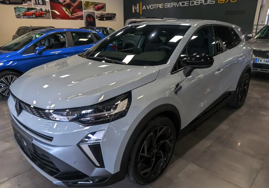 Renault Symbioz E-Tech gris Rafale en vue 3/4 avant droit, avec jantes noires et rétroviseurs noirs brillants.