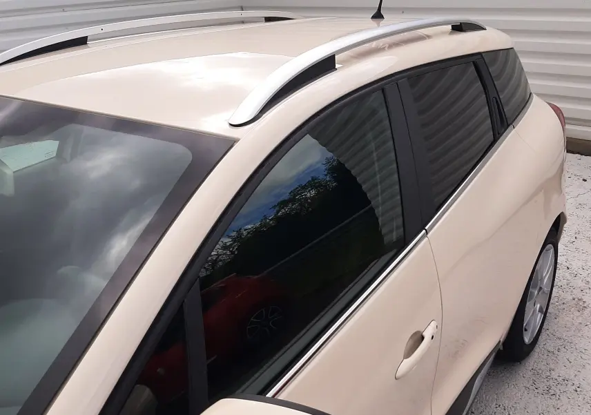 Vue 3/4 avant droit d'une Renault Clio IV Estate beige avec barres de toit et vitres teintées.