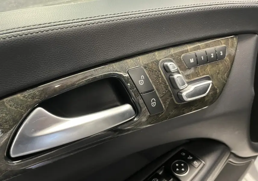Poignée intérieure côté gauche avec commandes de réglage sièges et mémoire sur panneau en bois foncé d'une Mercedes CLS 350 d gris.