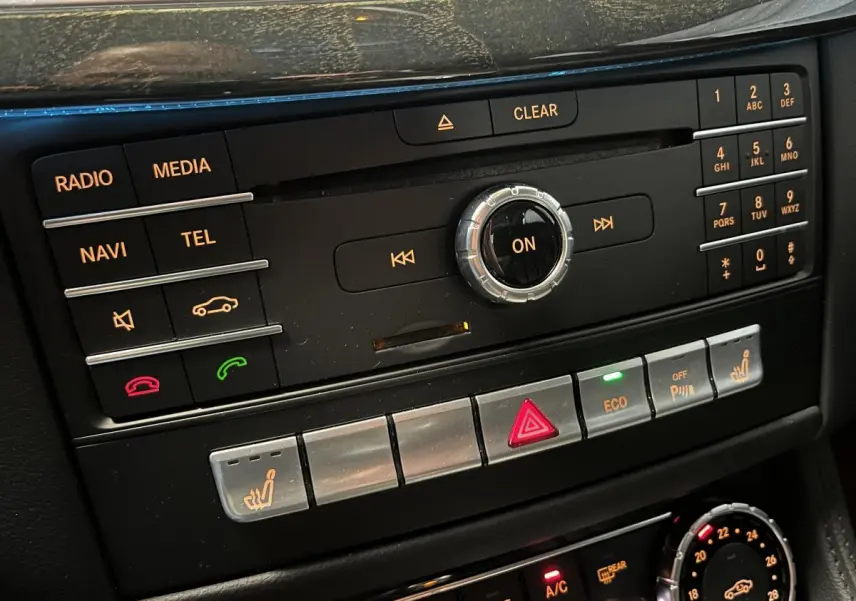 Console centrale de la Mercedes Classe CLS 350 d 2015 montrant les commandes multimédia et climatisation avec boutons rétroéclairés.