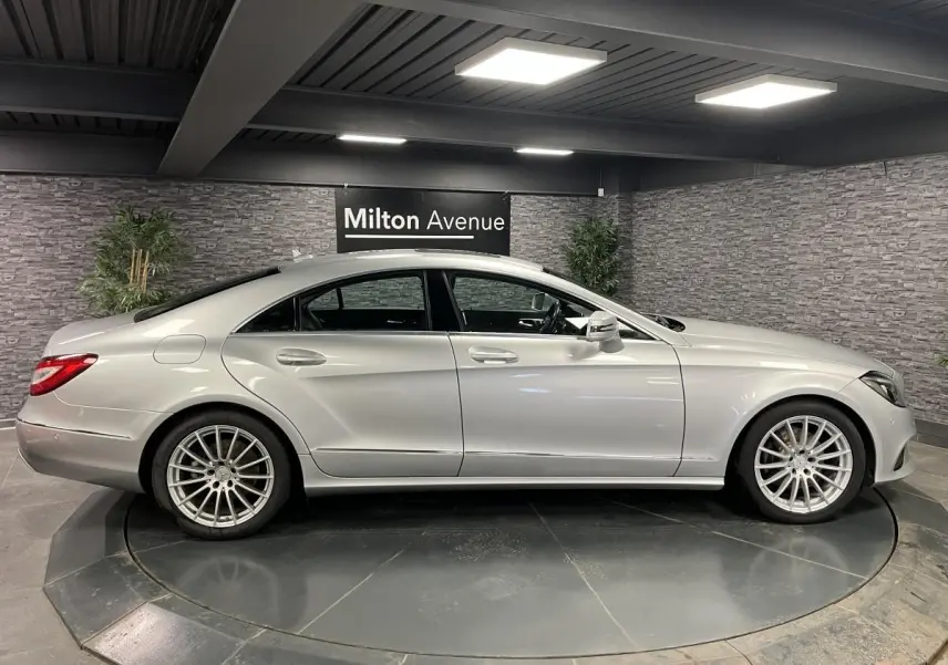 Profil côté gauche d'une Mercedes Classe CLS gris métallisé avec jantes alliage multibranches en showroom.