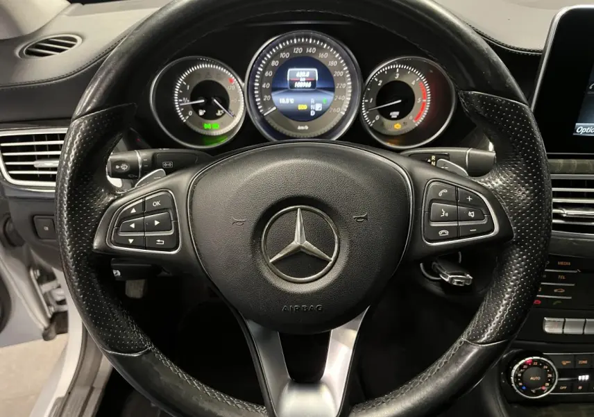Vue rapprochée du volant cuir noir perforé et du tableau de bord digital d'une Mercedes CLS 350 d gris de 2015.