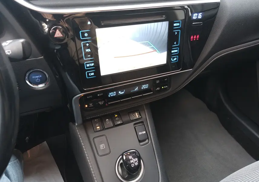 Vue intérieure centrée sur la console centrale et l'écran tactile de la Toyota Auris hybride blanche, avec levier de vitesses automatique.