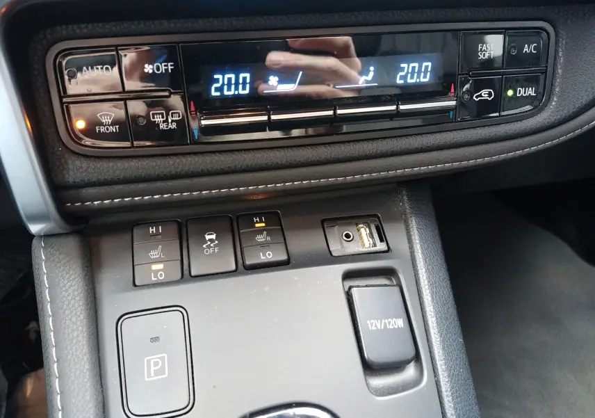 Vue rapprochée de la console centrale de la Toyota Auris hybride blanche, montrant les commandes de climatisation et sièges chauffants.