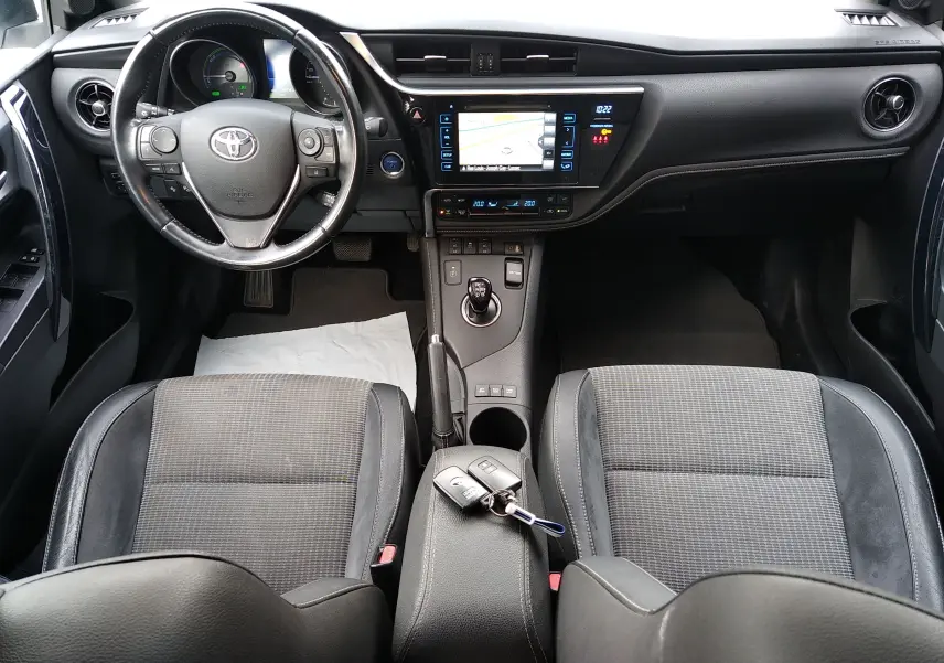 Vue intérieure avant de la Toyota Auris hybride 2016, avec tableau de bord noir et clés posées sur l'accoudoir central.
