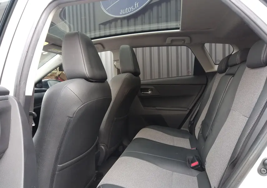 Vue intérieure arrière côté gauche d'une Toyota Auris hybride blanche, sièges tissu et cuir bicolores, toit ouvrant panoramique visible.