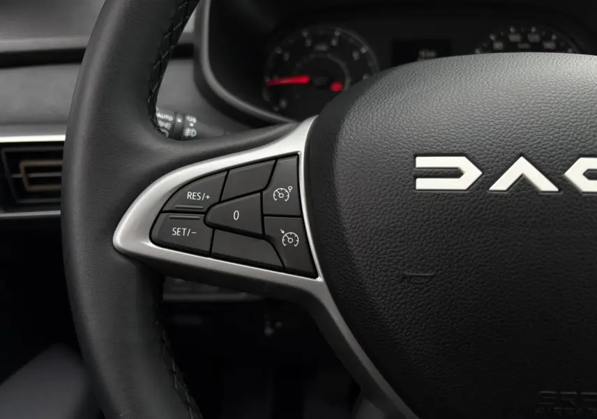 Gros plan sur le volant noir de la Dacia Sandero Stepway 2025 avec commandes de régulateur de vitesse intégrées.