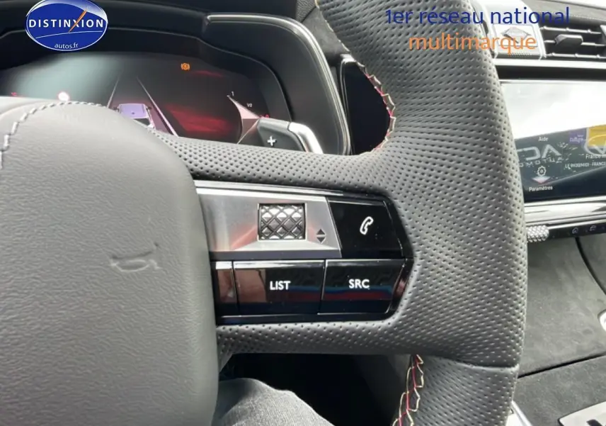 Gros plan sur le volant cuir perforé noir du DS7 1.5 BlueHDi 130 avec commandes au volant et écran tactile en arrière-plan.