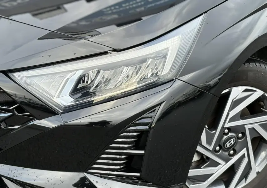 Gros plan sur l'avant droit noir Phantom Metal de la Hyundai i20 2025, mettant en valeur le phare et la jante alliage diamantée.