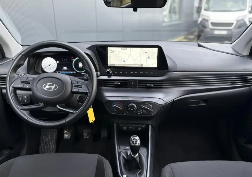 Vue intérieure avant de la Hyundai i20 2025 avec tableau de bord moderne, écran tactile GPS et volant cuir noir.
