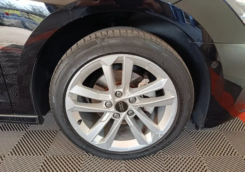 Gros plan sur la roue avant droite d’une Audi A3 noire 2023 avec jante alliage argentée et logo Audi au centre.