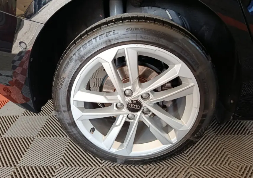 Gros plan sur la roue avant gauche noire d’une Audi A3 35 TDI 150 S tronic Business Line avec jante argentée à 5 branches doubles.