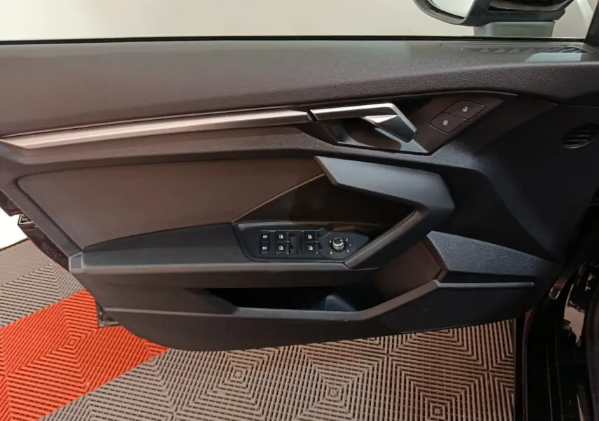 Vue intérieure côté gauche de la porte noire d’une Audi A3 35 TDI 150 S tronic Business Line avec commandes de vitres et rétroviseurs.