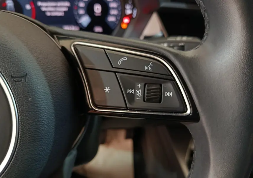 Gros plan sur les commandes vocales et audio au volant cuir de l'Audi A3 35 TDI noir, tableau de bord numérique en arrière-plan.