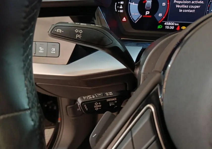 Gros plan sur le volant cuir et les commandes au volant côté gauche de l’Audi A3 35 TDI noire avec tableau de bord digital.