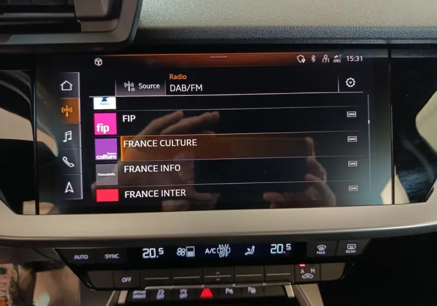Écran tactile central de l’Audi A3 Business Line 2023 affichant les stations radio DAB/FM, avec commandes climatisation en dessous.