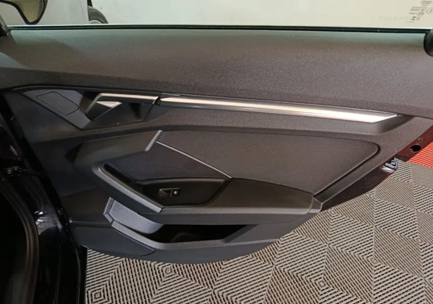 Vue rapprochée de la porte avant gauche noire d’une Audi A3 35 TDI 150 S tronic Business Line avec garniture moderne et poignée argentée.