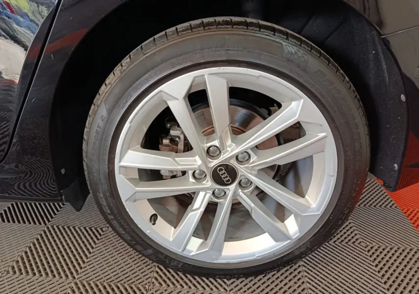 Gros plan sur la roue avant droite d'une Audi A3 noire, jante alliage argentée à 5 doubles branches.