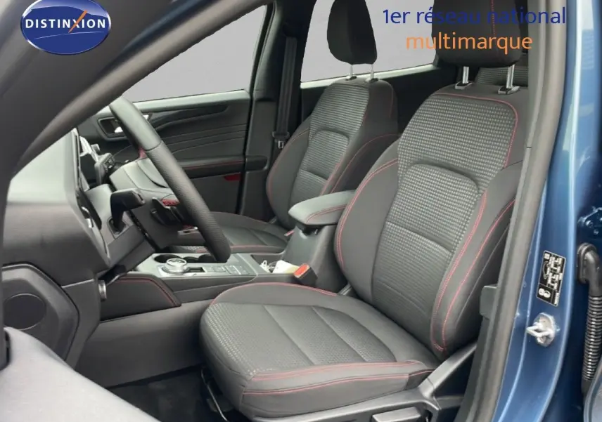 Vue intérieure côté conducteur du Ford Kuga bleu Vapor Metal 2024, sièges tissu noir avec surpiqûres rouges visibles.