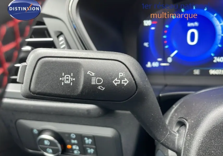 Gros plan sur la commande de clignotants et feux du Ford Kuga 2024, intérieur noir avec tableau de bord numérique bleu.