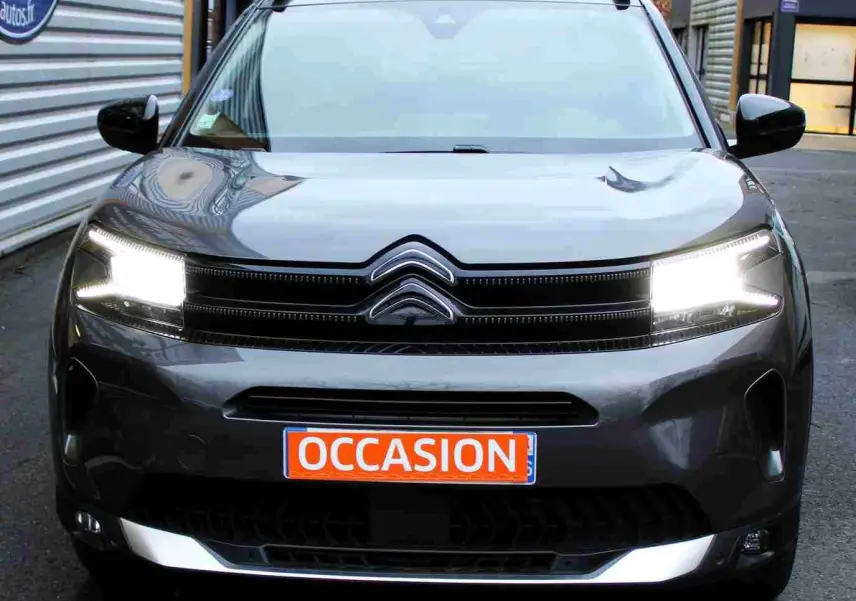 Vue frontale d'un Citroën C5 Aircross gris platinium avec phares allumés et plaque "OCCASION" orange visible.