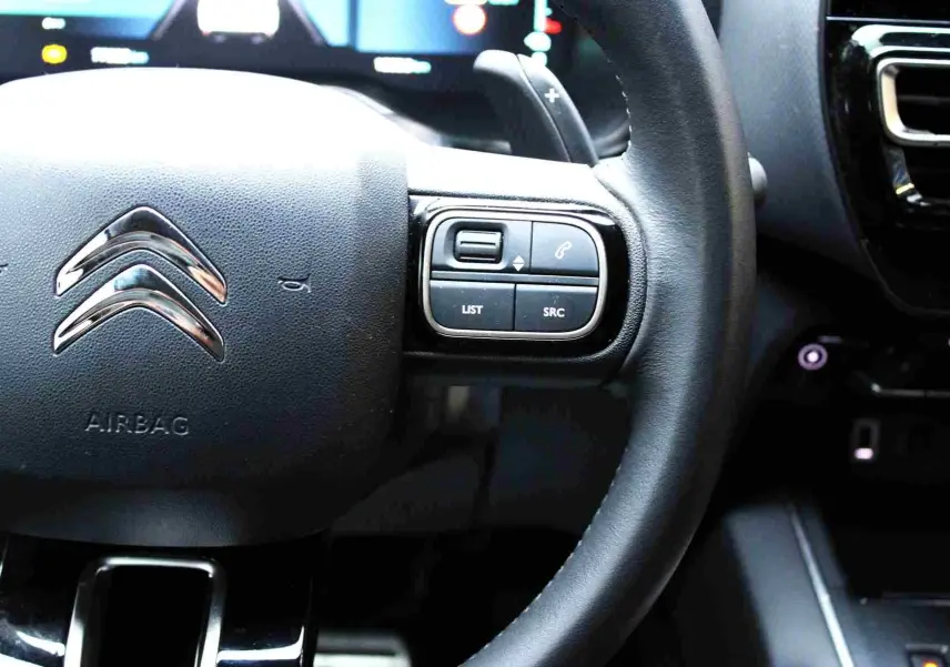 Gros plan sur le volant noir du Citroën C5 Aircross hybride avec commandes intégrées côté droit.