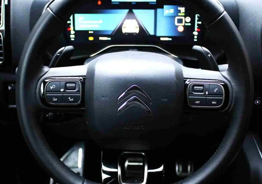 Vue rapprochée du volant noir de la Citroën C5 Aircross hybride rechargeable avec tableau de bord numérique lumineux.