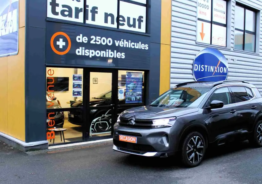 Vue 3/4 avant d'un Citroën C5 Aircross gris platinium hybride rechargeable garé devant un concessionnaire.