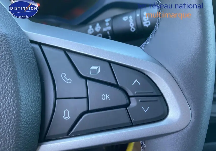 Gros plan sur les commandes multifonctions noires du volant du Dacia Duster 2025, avec boutons de navigation et appel.