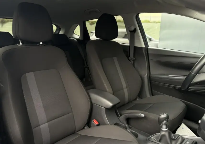 Vue intérieure côté droit de la Hyundai i20 2025, sièges tissu noirs avec accoudoir central et levier de vitesses manuel.