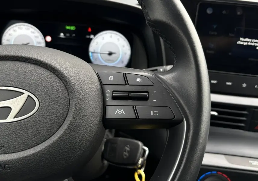 Gros plan sur le volant cuir de la Hyundai i20 2025 avec commandes au volant et tableau de bord numérique.