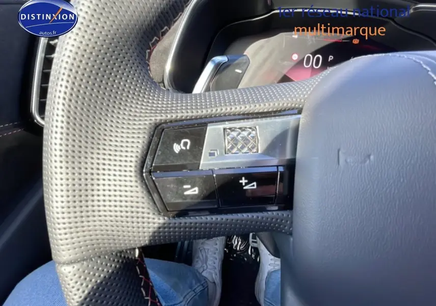 Gros plan sur le volant cuir perforé du DS7 bleu 1.5 BlueHDi 130, avec commandes intégrées et coutures rouges visibles.