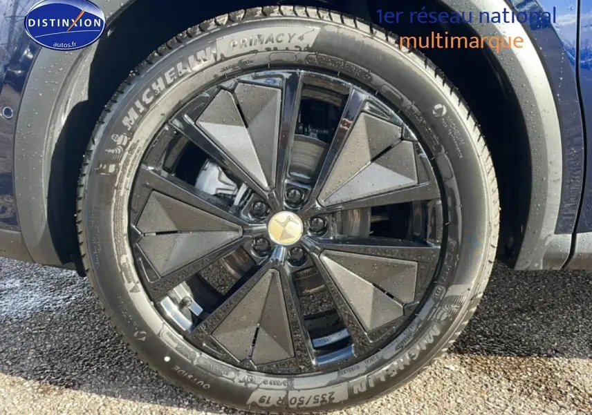 Gros plan sur la roue avant droite d’un DS7 bleu, jante alliage noire au design géométrique distinctif.