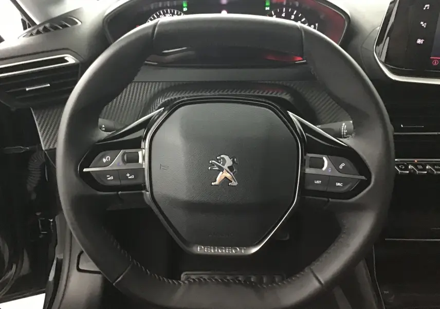 Vue rapprochée du volant cuir noir du Peugeot 208 2022 avec commandes intégrées et tableau de bord en arrière-plan.