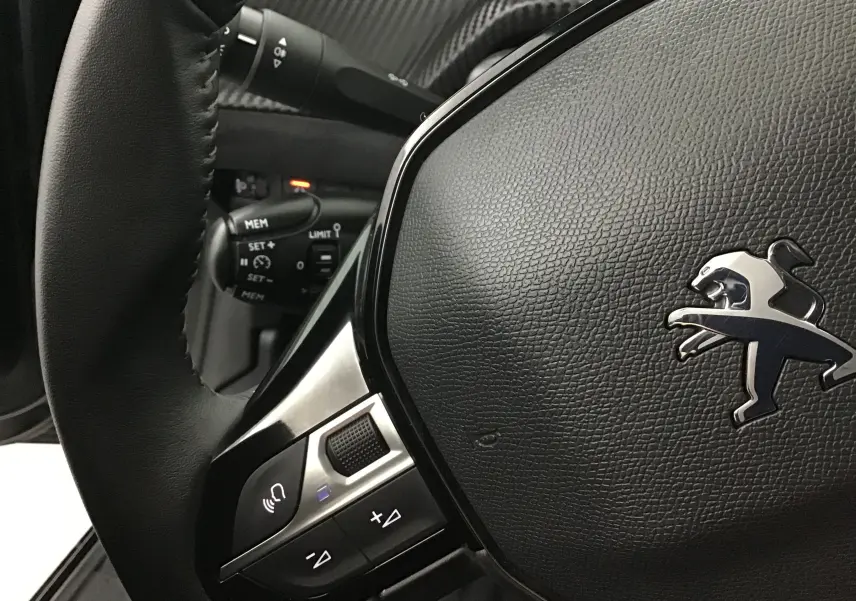 Gros plan sur le volant en cuir noir de la Peugeot 208 2022, avec commandes intégrées et logo lion argenté.