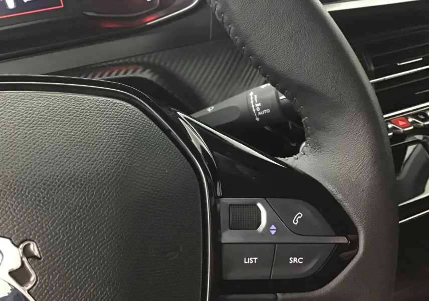 Gros plan sur le volant cuir noir de la Peugeot 208 2022, avec commandes audio et téléphone intégrées.