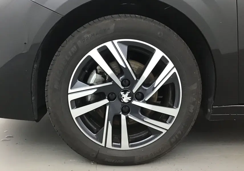 Gros plan sur la jante alliage bicolore avec logo Peugeot d'une 208 noire, côté arrière droit.