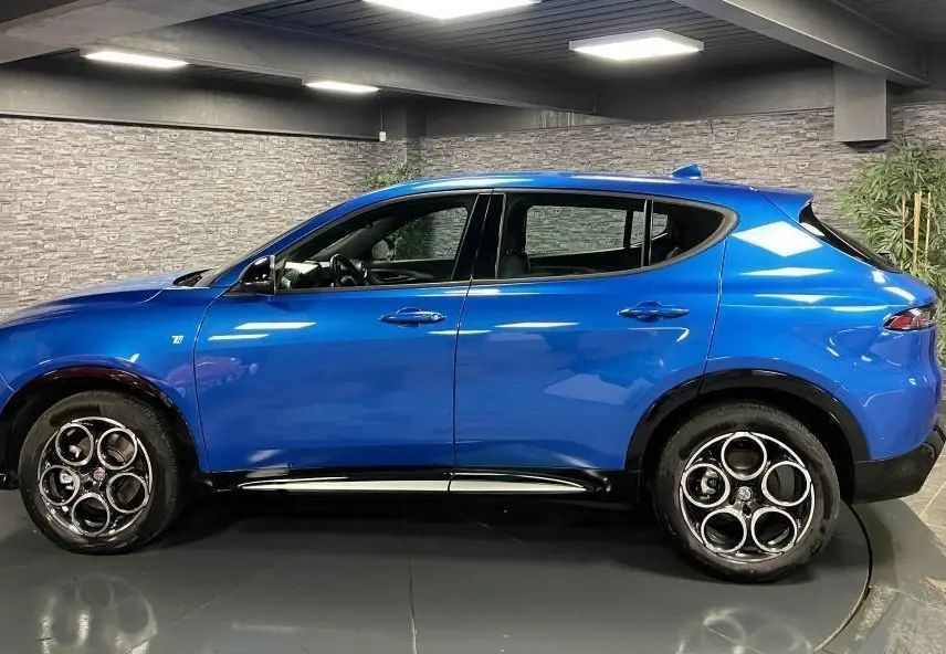 Profil droit de l'Alfa Romeo Tonale 1.5 mHEV 160 TI bleu métallisé avec jantes alliage 18 pouces en intérieur showroom.