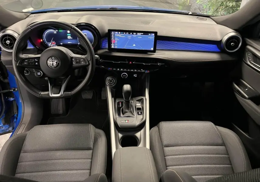 Vue intérieure avant de l'Alfa Romeo Tonale bleu, tableau de bord noir avec écran tactile et éclairage d'ambiance bleu.