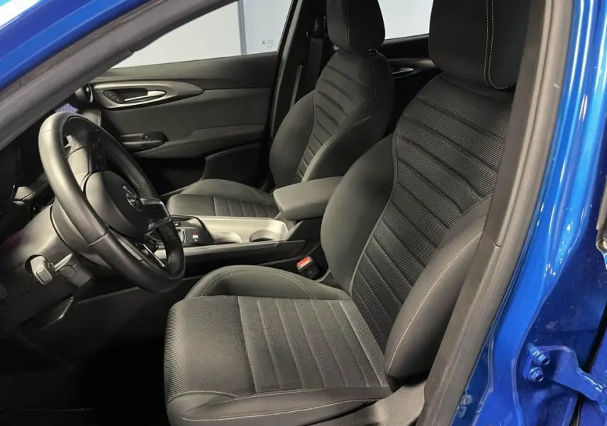 Vue intérieure côté conducteur de l'Alfa Romeo Tonale bleu 2024, sièges AlfaTec noirs avec surpiqûres beige et volant cuir.